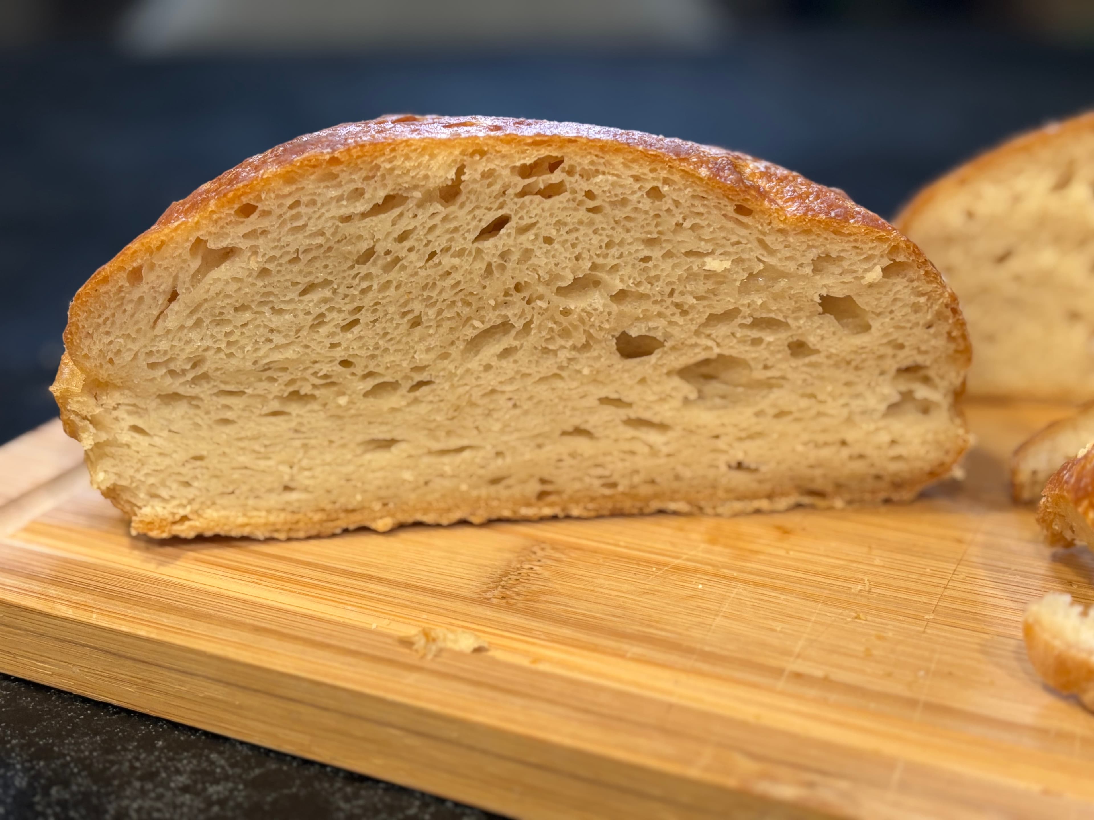 Round loaf of no-knead gluten-free bread with a deep golden crust, one slice cut to show the open crumb